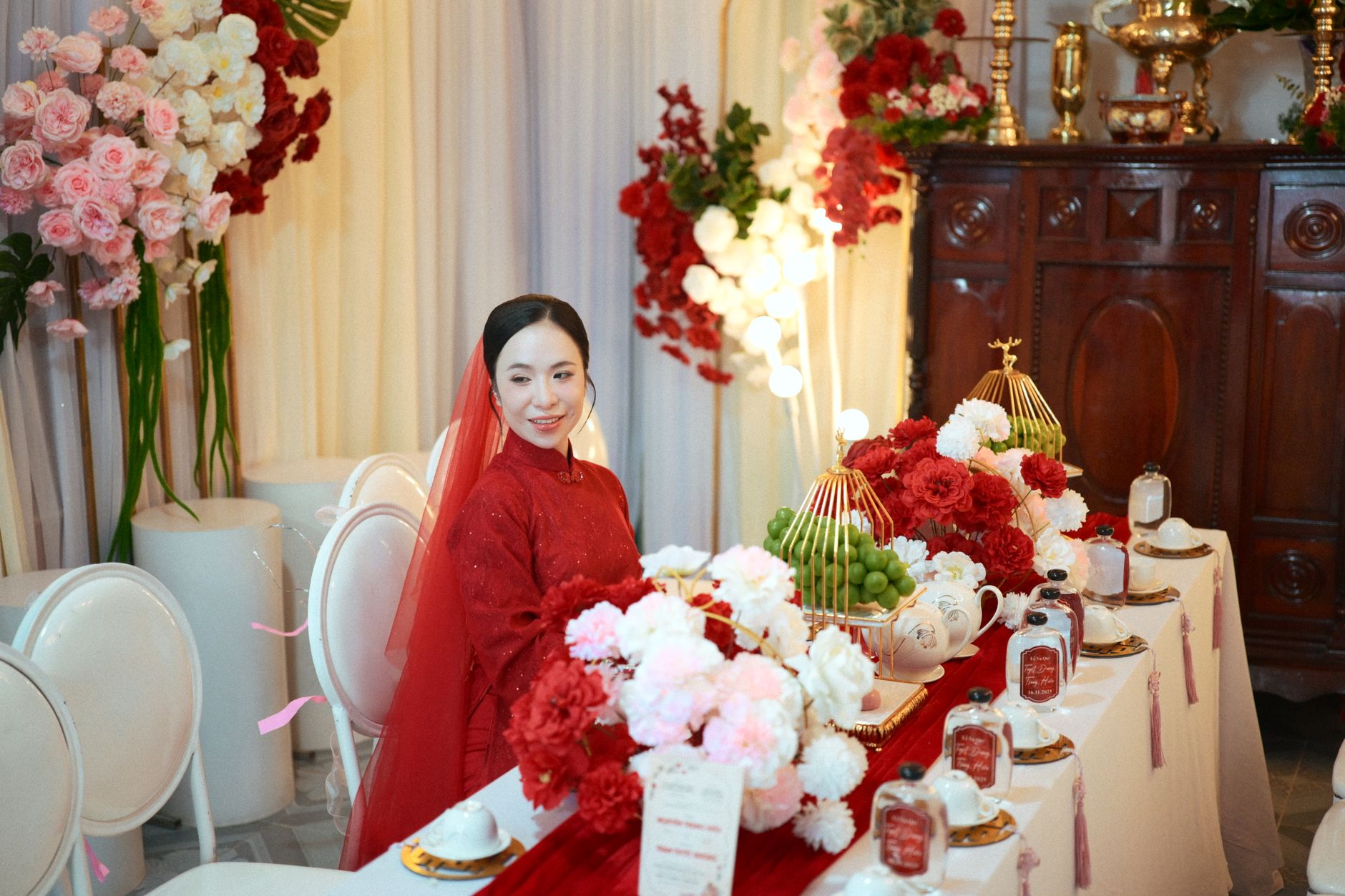 Asian bride in traditional red dress at luxurious wedding table with floral arrangements.
