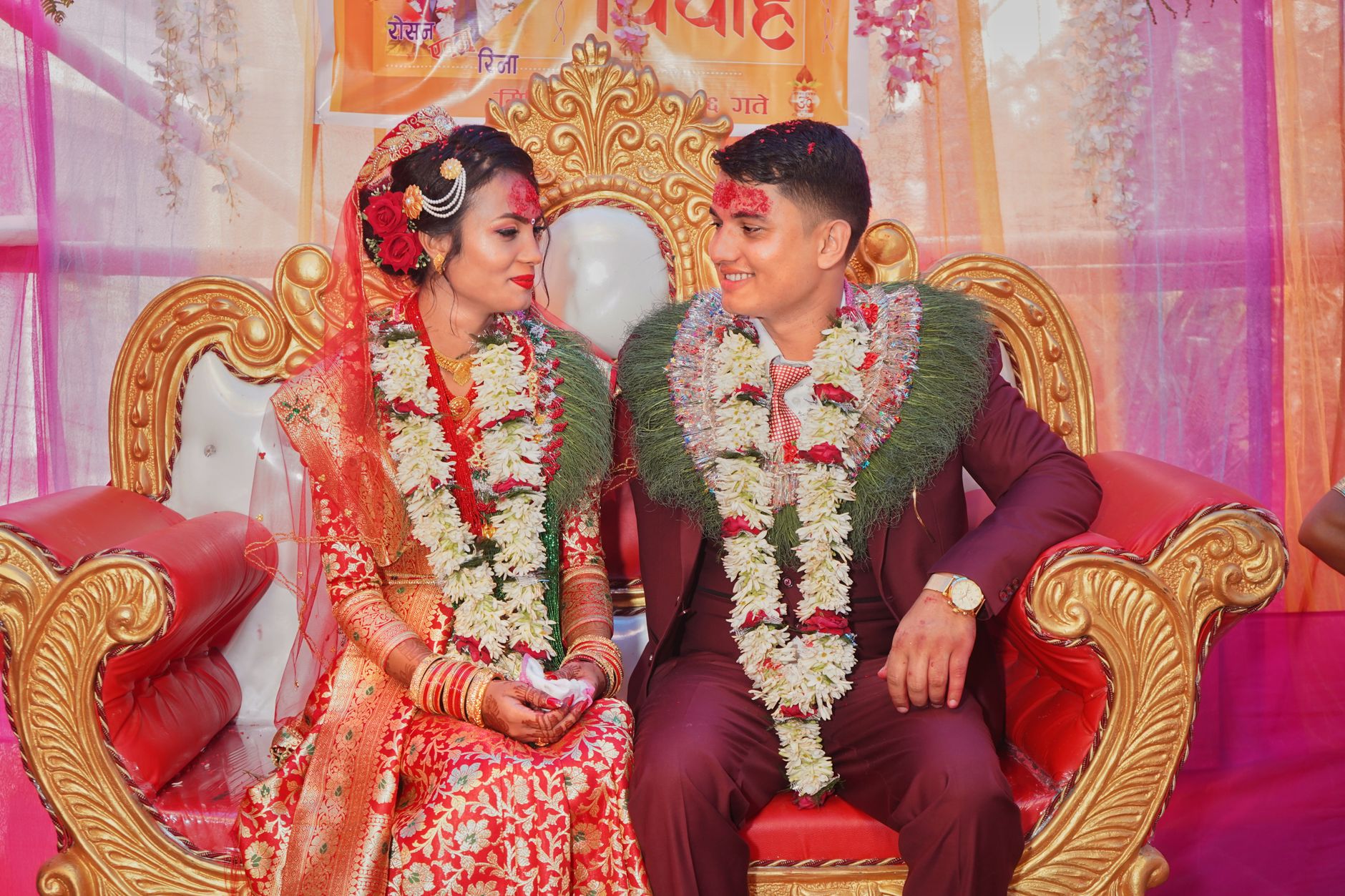 A joyful couple in traditional South Asian attire celebrating their wedding with vibrant decor.