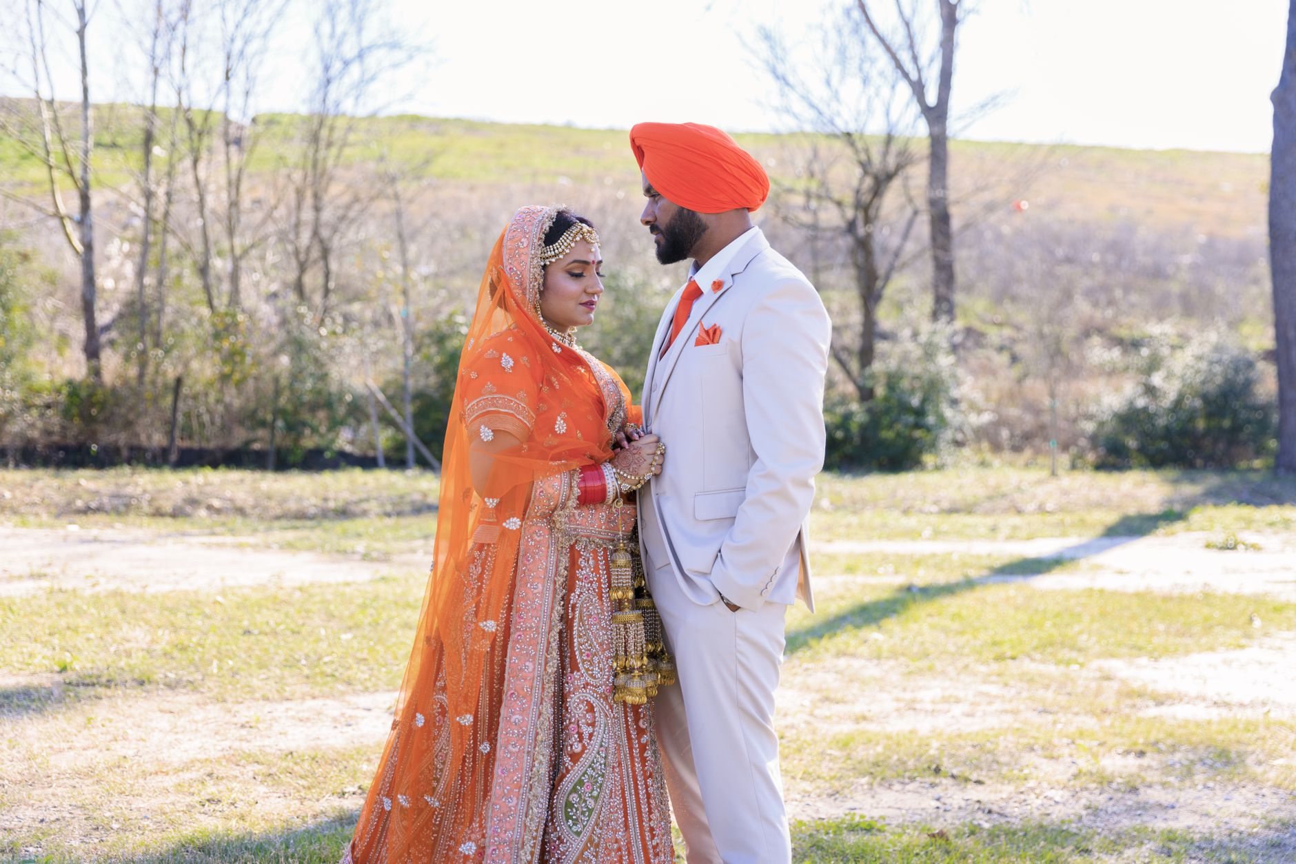 A South Asian couple in traditional attire poses outdoors on their wedding day.